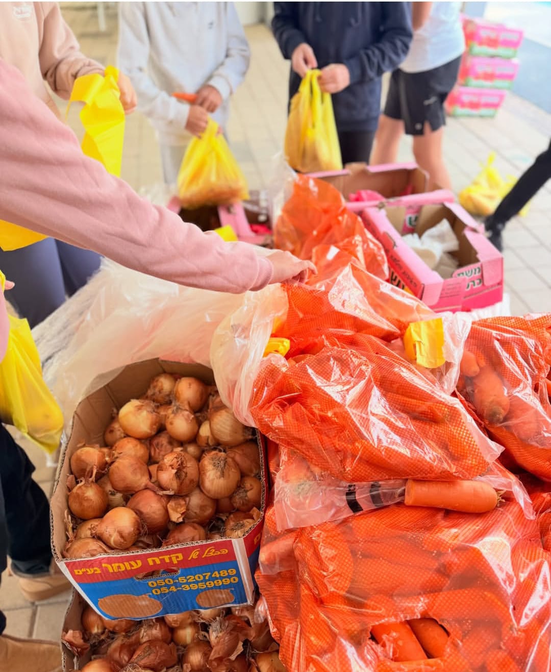 Students preparing produce bags beside boxes of onions and sacks of carrots