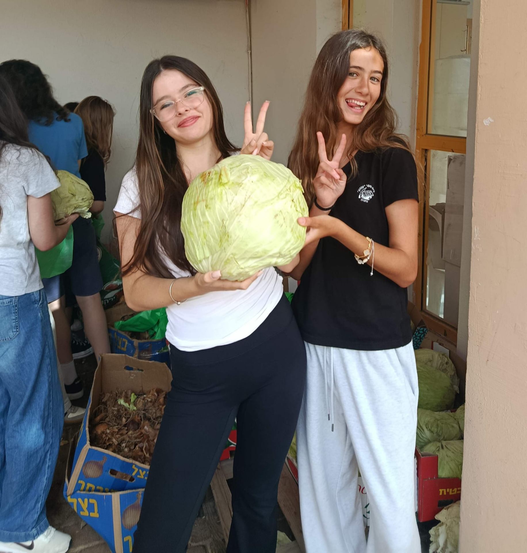 Two students holding a cabbage beside produce crates