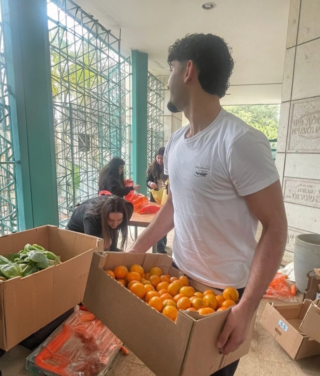 Participant carrying a crate of oranges beside other fresh produce
