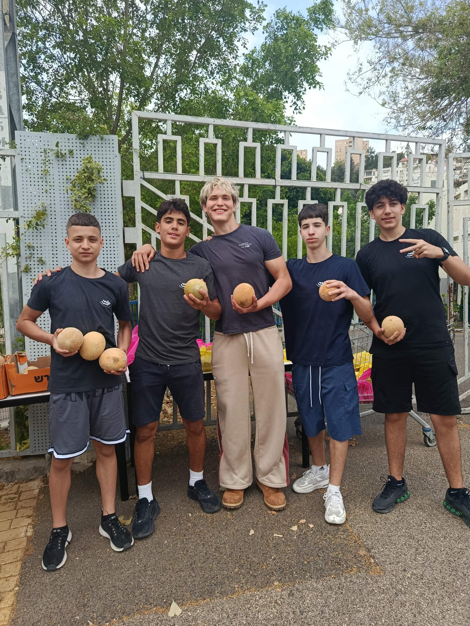 Five students holding melons beside packed produce bags